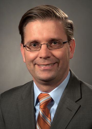 Kristofer Smith, MD, wearing a brown suit and orange tie